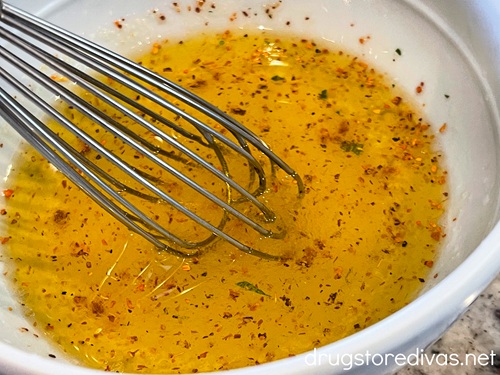 A small whisk in a light blue bowl that has an orange salad dressing in it.