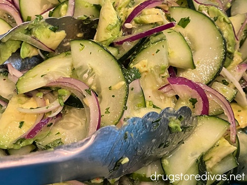 Silver tongs with cilantro, avocado, red onion, and cucumber.