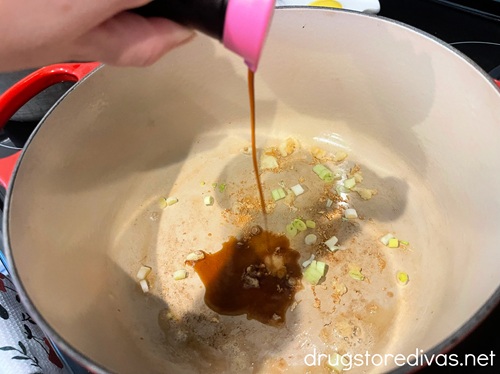 Soy sauce being poured into a Dutch oven that has garlic and green onion in the bottom.