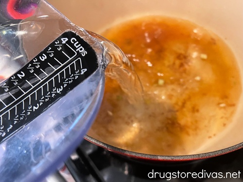 Water being poured from a measuring cup into a Dutch oven with brown liquid in the bottom.