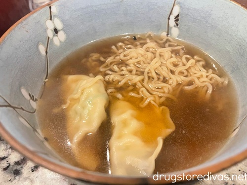 Two gyoza, ramen noodles, and broth in a blue bowl.
