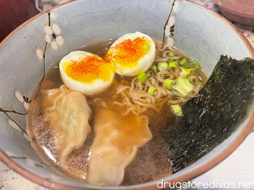 A jammy egg cut open with toharashi on top in a bowl of broth with two gyoza, ramen noodles, green onion, and a piece of seaweed.