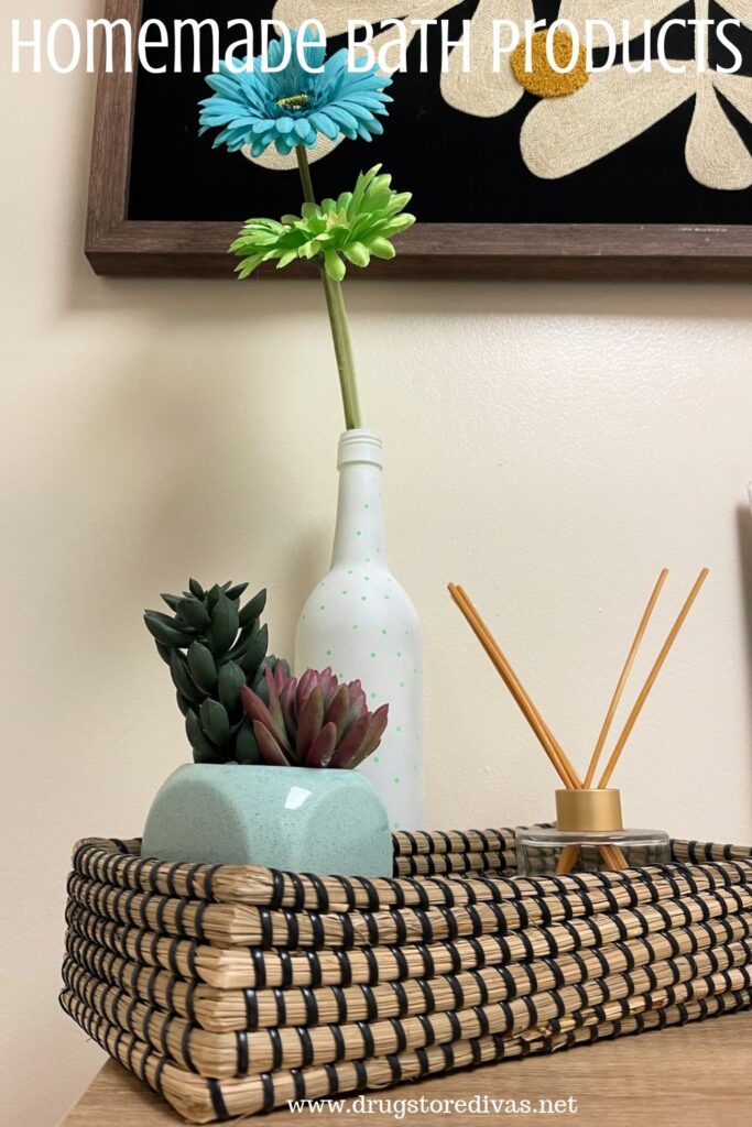 A small basket with a fake flower and plant and reed diffuser in a bathroom with the words "Homemade Bath Products" digitally written on top.