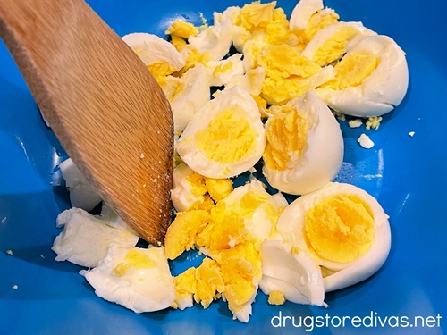 A bamboo spoon breaking up hard boiled eggs in a blue bowl.