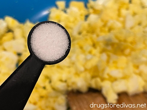 Salt in a measuring spoon above a bowl of mashed hard boiled eggs.