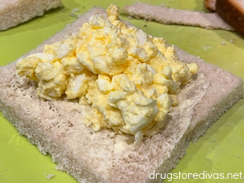 Egg salad on a square piece of crustless bread.