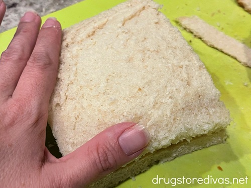 A hand squishing down the edges of a piece of white bread with the crust cut off.