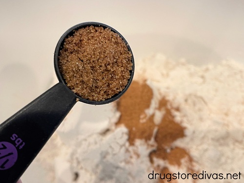 A measuring spoon with brown sugar over a bowl with white and orange dry powders in the bottom.
