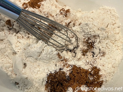 A small whisk in a white bowl with white and brown powder at the bottom.
