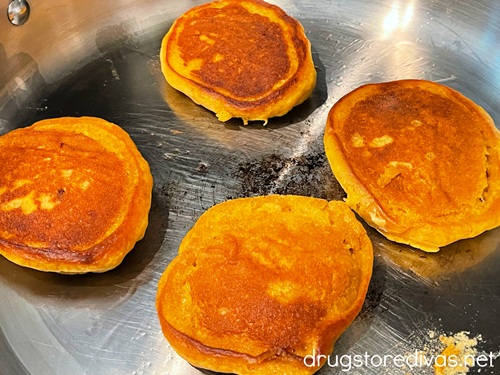 Four cooked pancakes in a silver skillet.