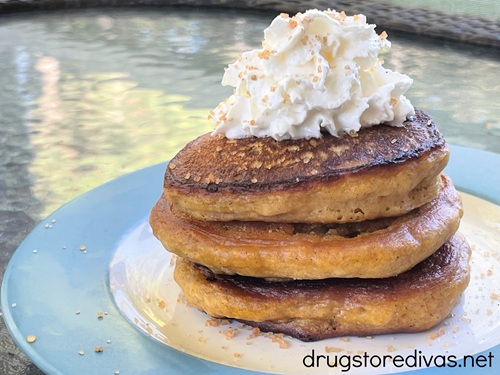 Three pumpkin pancakes with whipped cream and sugar on top on a white and blue plate.