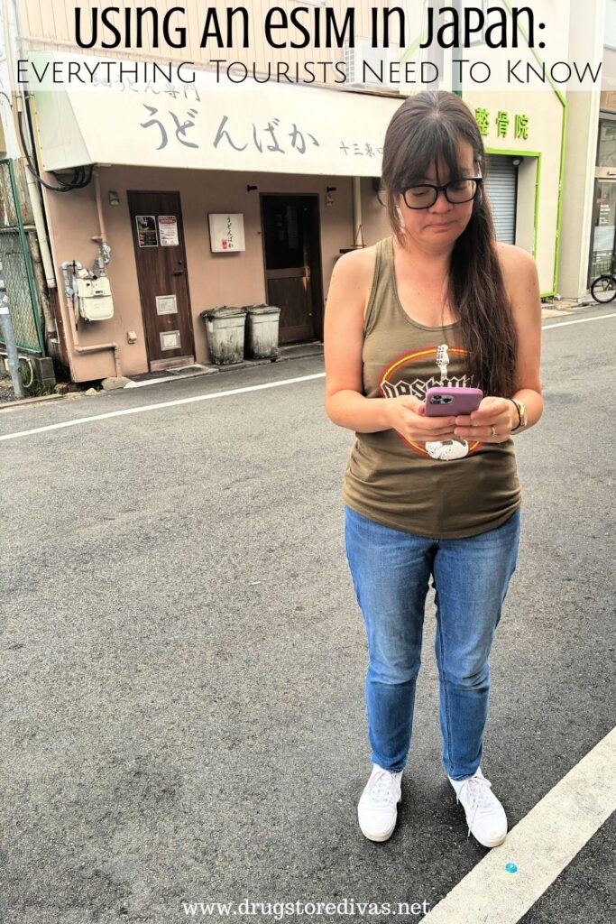 A woman in jeans and a tank top, looking at her phone, on a Japanese street with the words "Using An eSIM In Japan: Everything tourists need to know" digitally written above her.